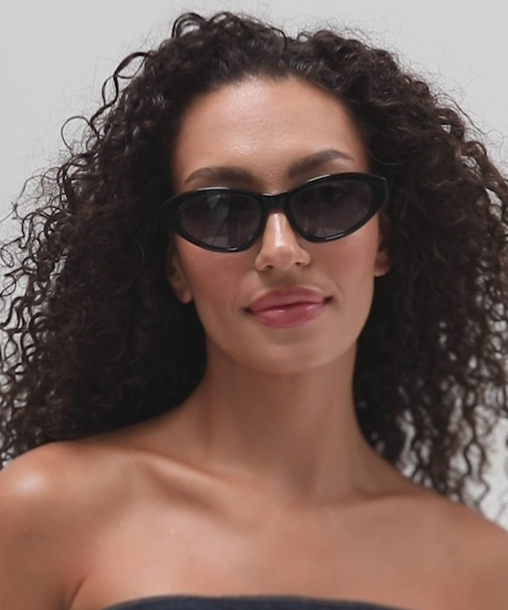 Woman wearing black colored cat eye sunglasses and a denim top, posing against a white background #color_black