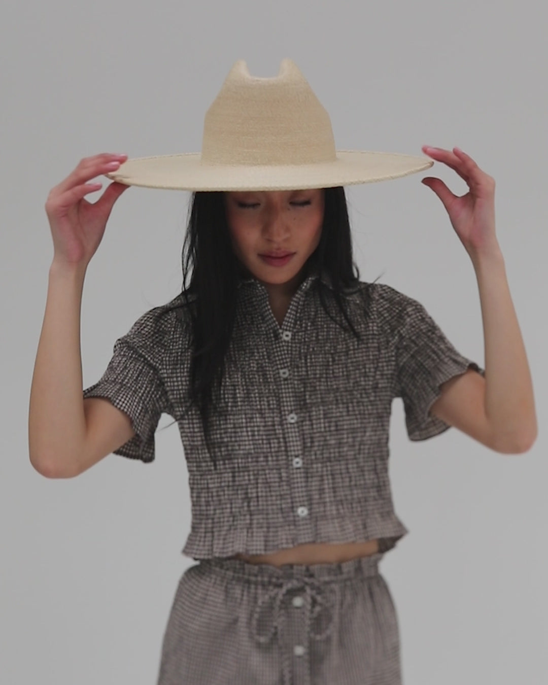 Woman wearing a natural colored western wide brim straw hat and a grey outfit against a plain background #color_natural