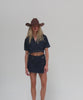 Woman wearing a chocolate colored cowboy hat, a dark blue denim shirt and a dark blue denim skirt, posing against a plain background #color_chocolate