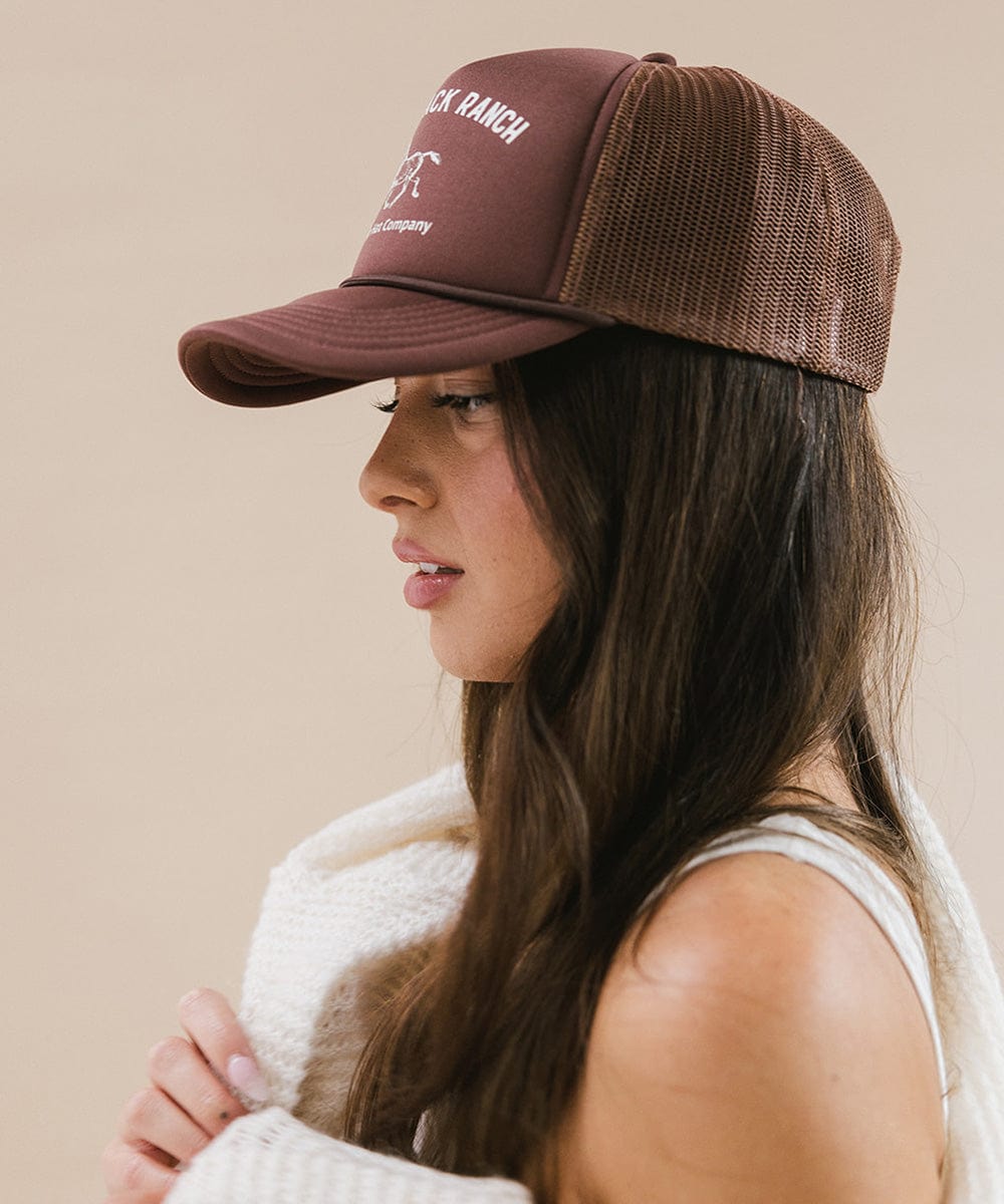 Woman wearing chocolate brown cap   and a white top, facing sideways against a plain background  #color_chocolate brown
