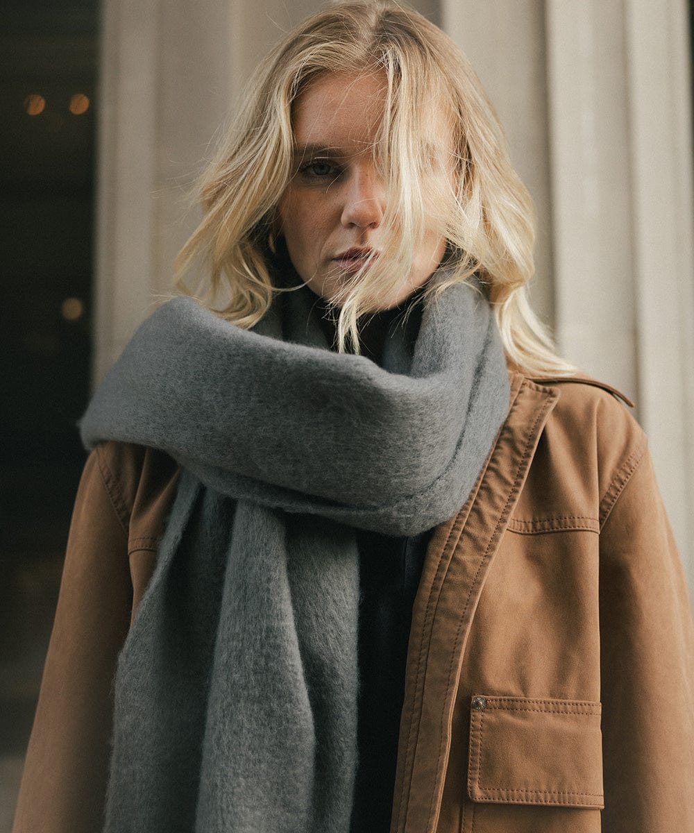 A person wearing a brown jacket and a grey oversized knit scarf, draped over the neck against a plain background  #color_grey