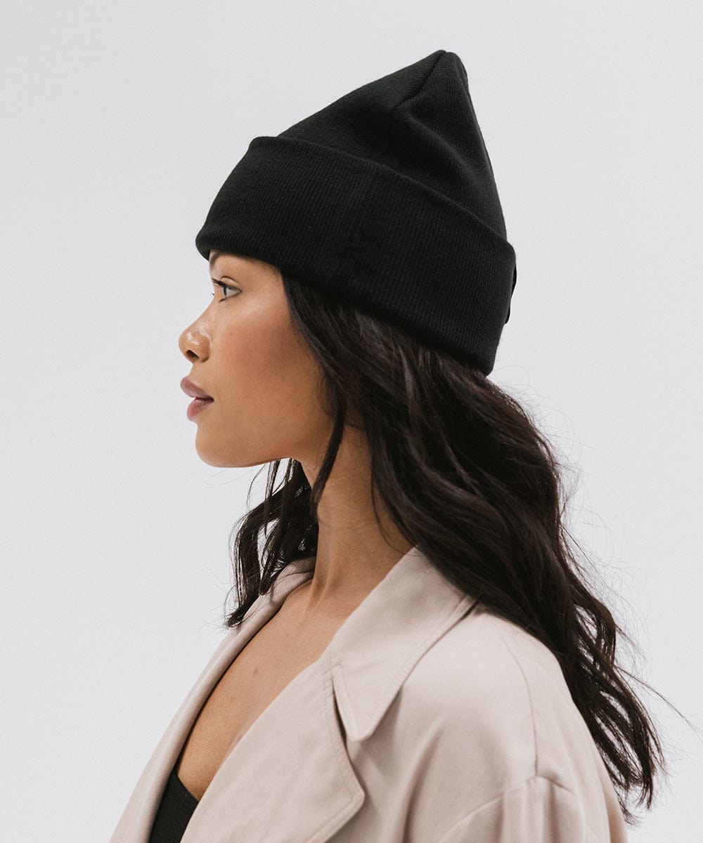 Woman wearing a black beanie and a  cream coat, facing sideways against a plain background #color_black