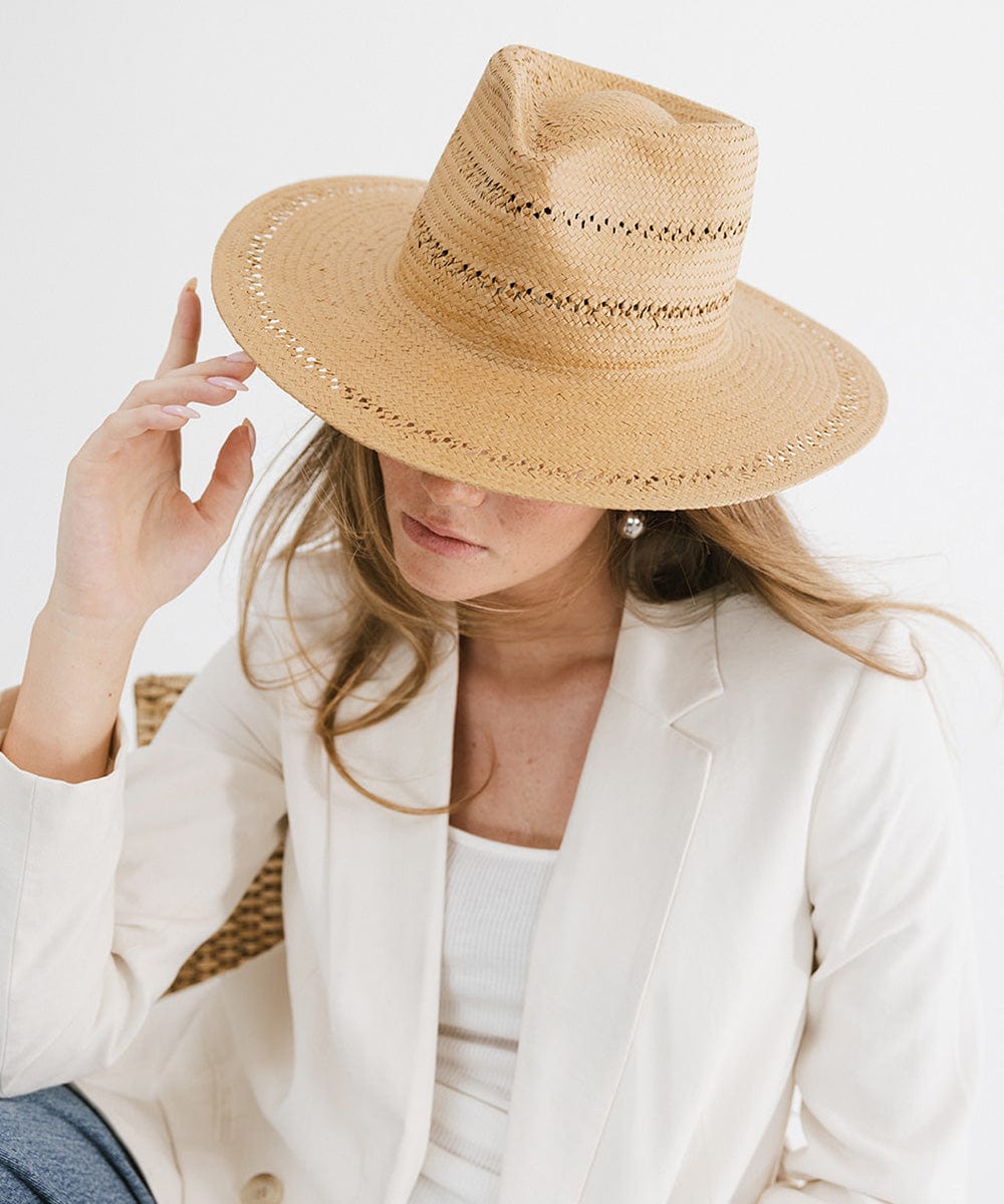 Woman wearing a honey colored teardrop straw fedora hat and a white top with a white blazer, posing against a plain background #color_honey