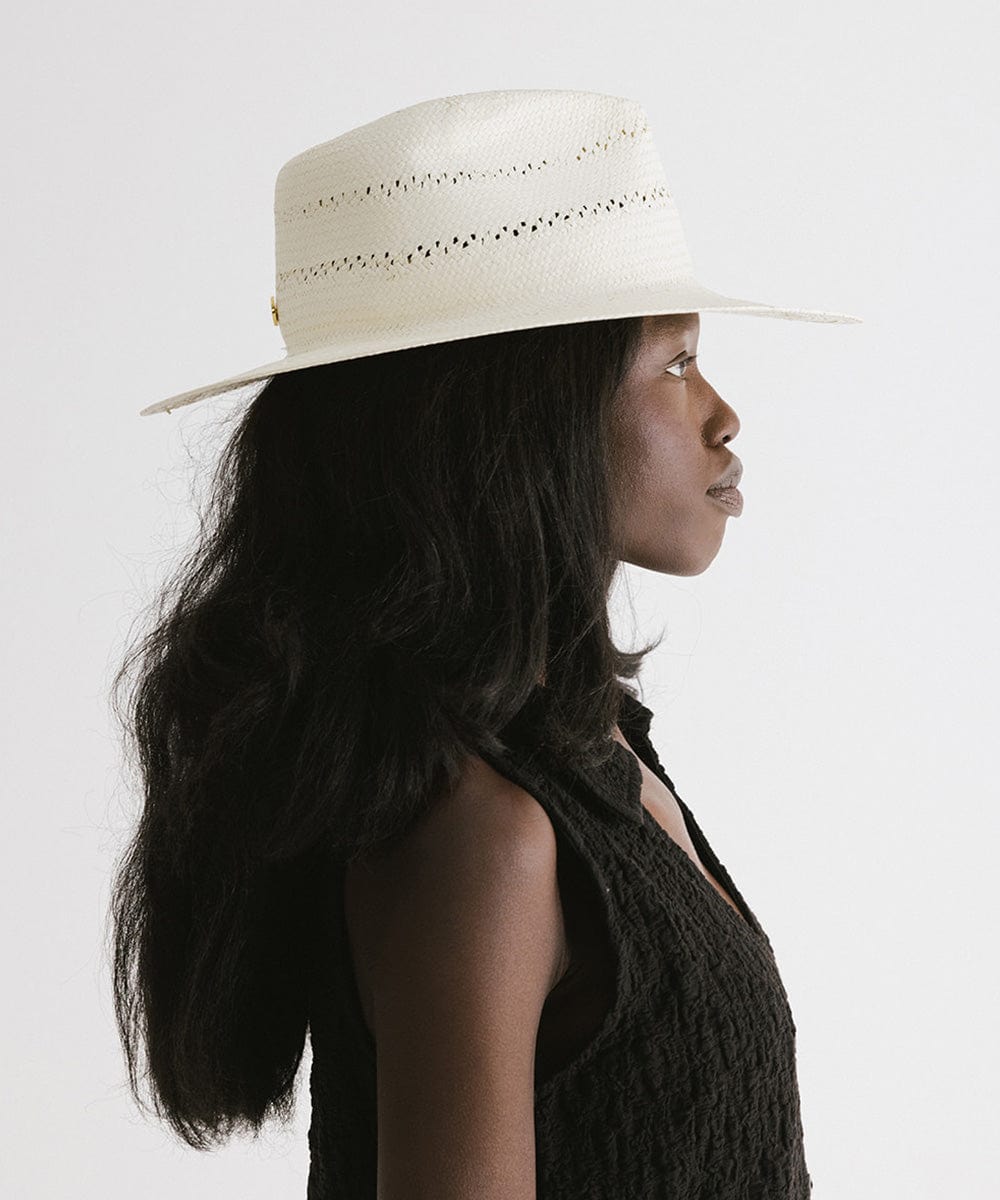 Woman wearing a white straw fedora hat with decorative trim and a black top, facing sideways against a plain background  #color_white