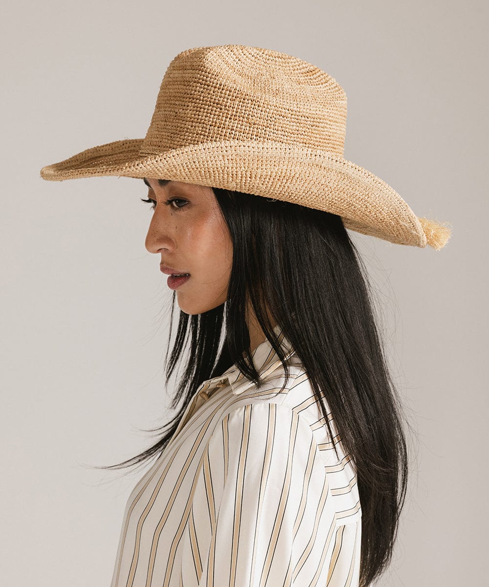 Woman wearing a natural colored straw cowboy hat and a light colored shirt, facing sideways against a plain background #color_natural