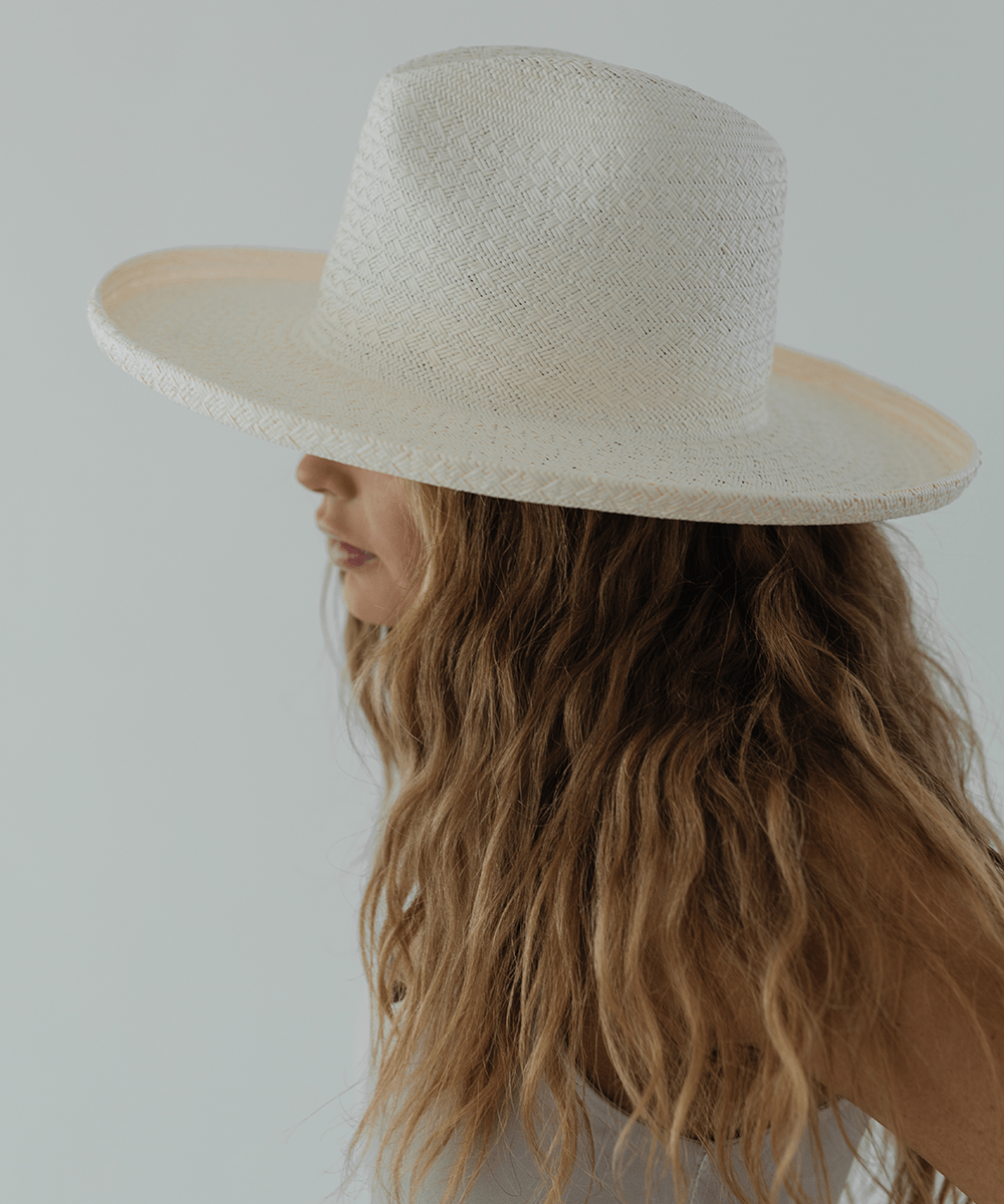 Woman wearing a white pencil brim straw hat facing sideways against a plain background #color_white
