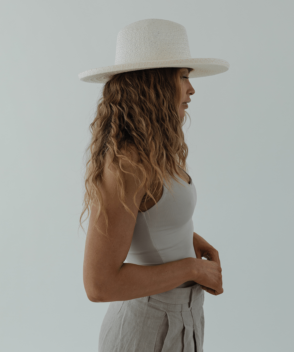 Woman wearing a white pencil brim straw hat and a white top, facing sideways against a plain background #color_white