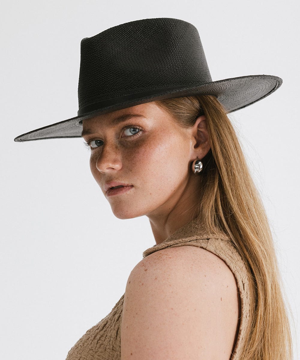 Woman wearing a black straw hat with a hat band and a beige top against a plain background #color_black