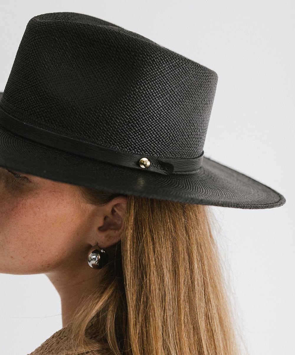 Woman wearing a black straw hat with a hat band and big earrings, facing sideways  against a plain background #color_black