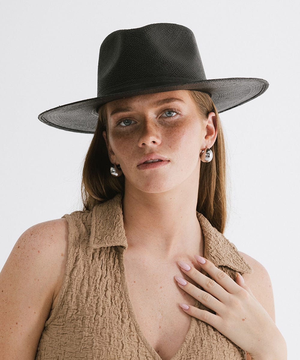 Woman wearing a black straw hat with a hat band and a beige top against a plain background #color_black