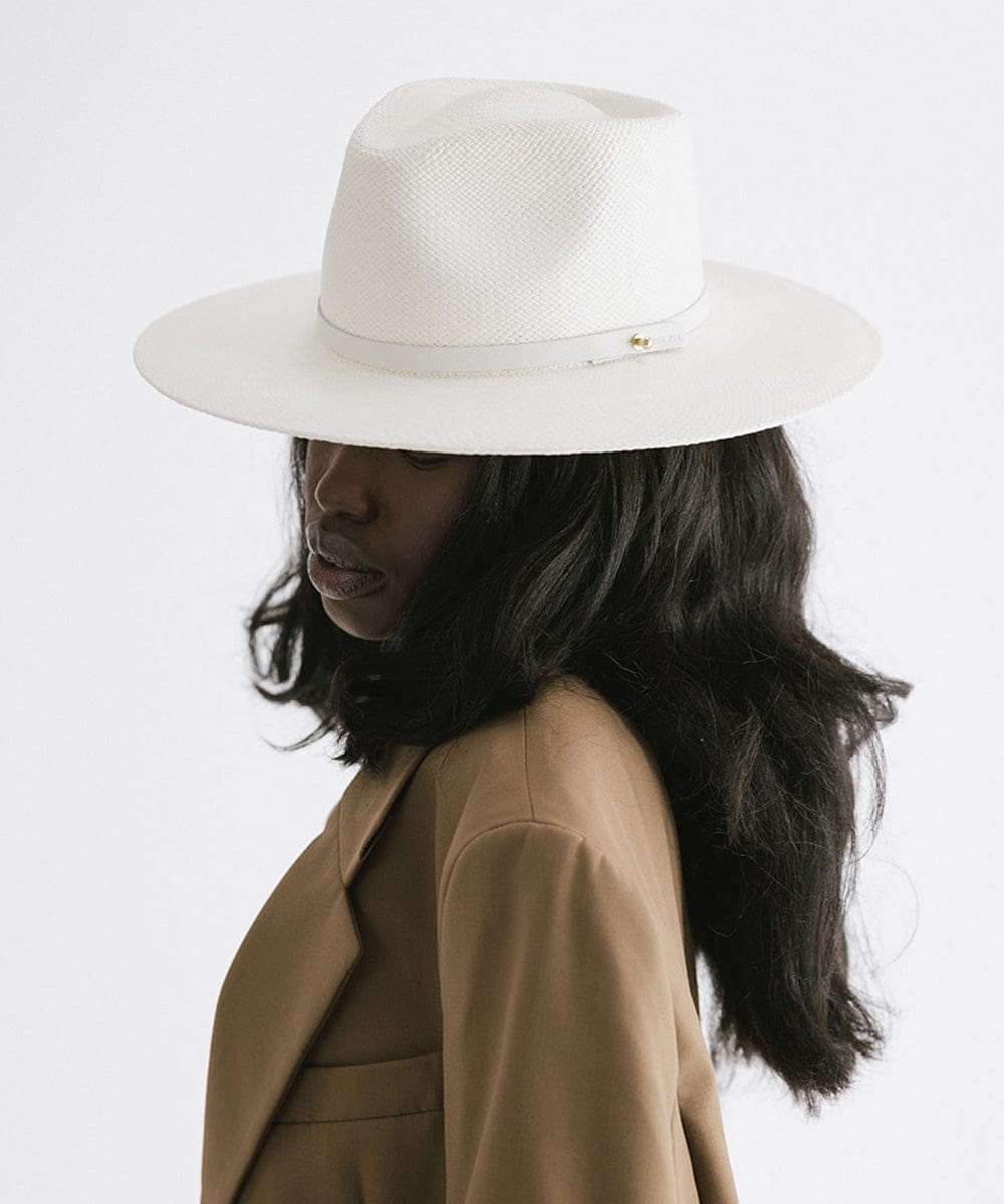 Woman wearing a white straw hat with a hat band and a brown coat, facing sideways against a plain background #color_white