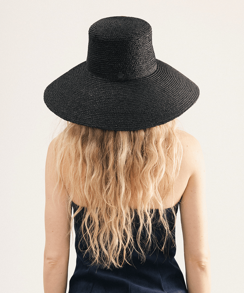Woman wearing a black oversized raffia straw bucket hat with a wide brim on a white background #color_black