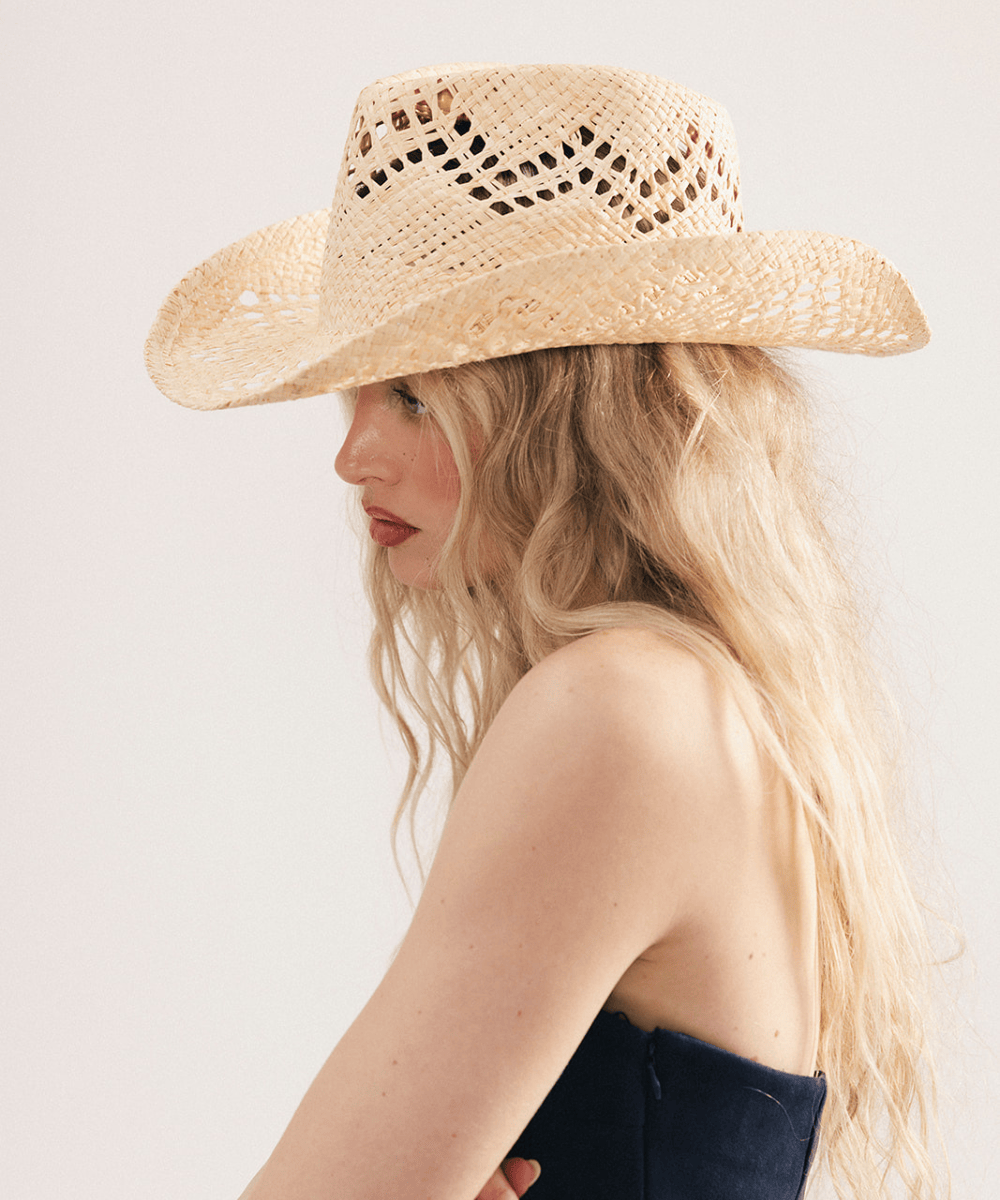 Woman wearing a natural colored straw cowboy hat and dark clothing against a plain background #color_natural
