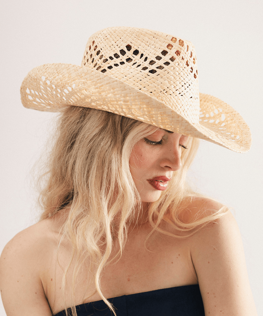 Woman wearing a natural colored straw cowboy hat and dark clothing against a plain background #color_natural