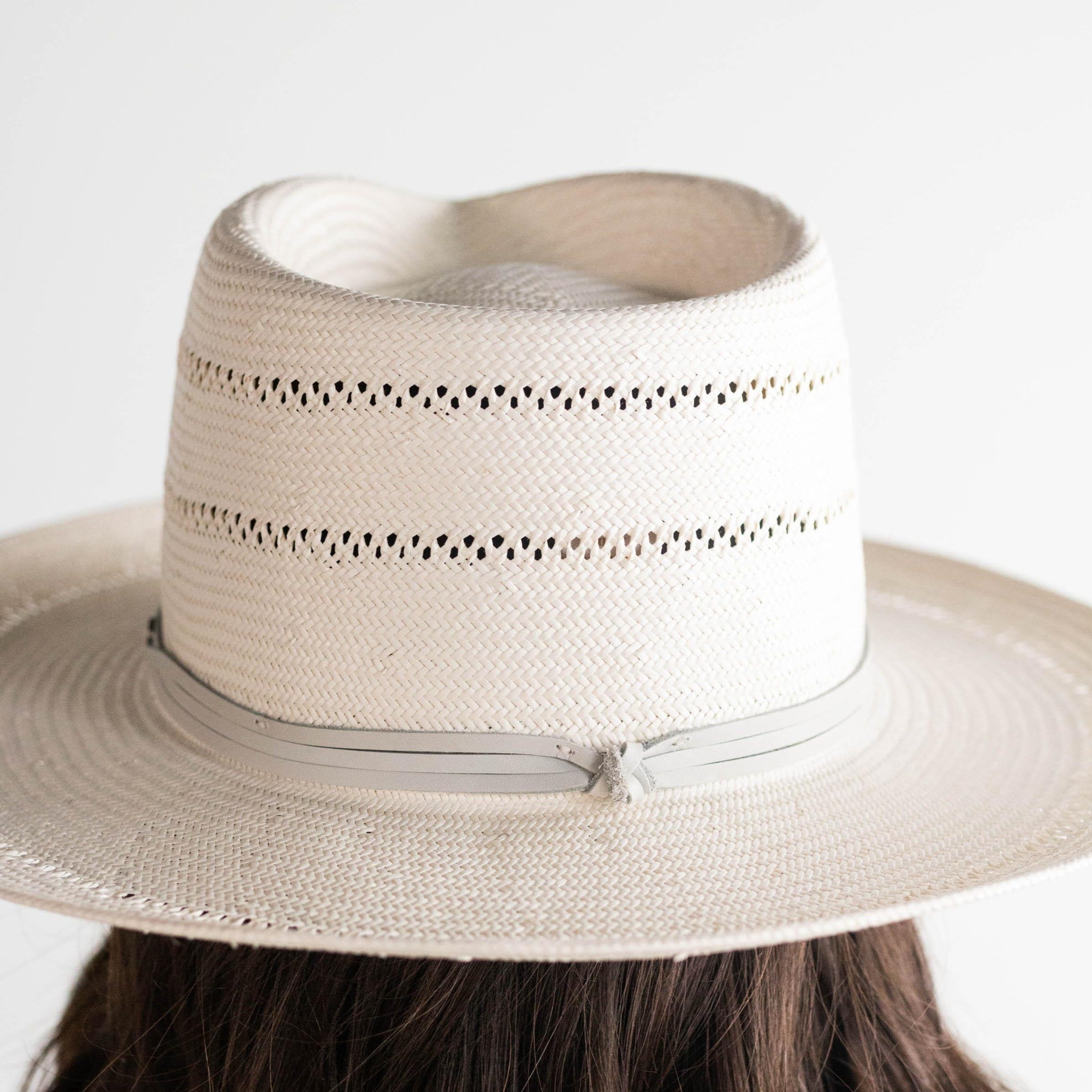 A grey straw fedora hat with a hat band worn by a person on a plain background #color_grey