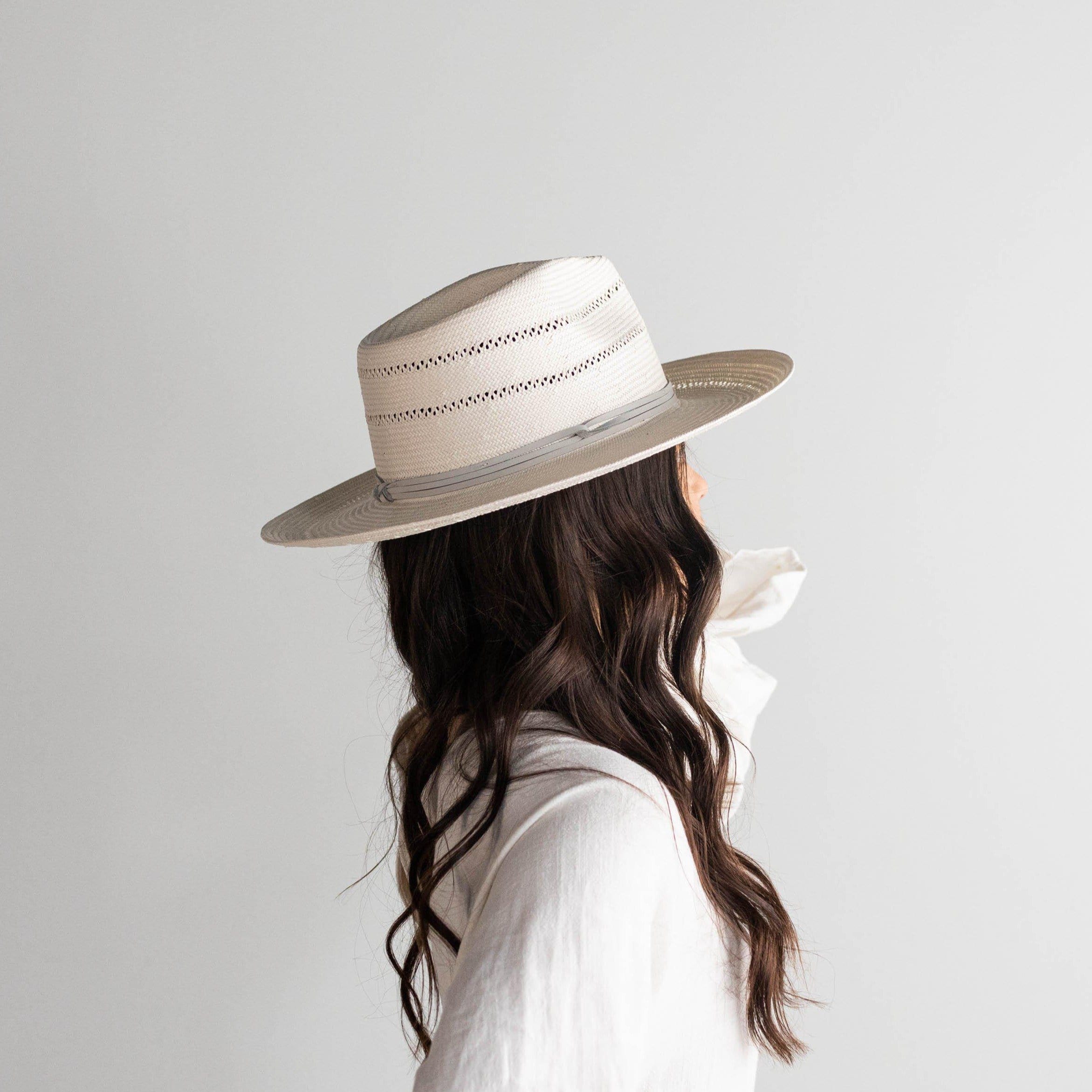 Woman wearing a grey straw fedora hat with a hat band and a white top, facing behind against a plain background #color_grey