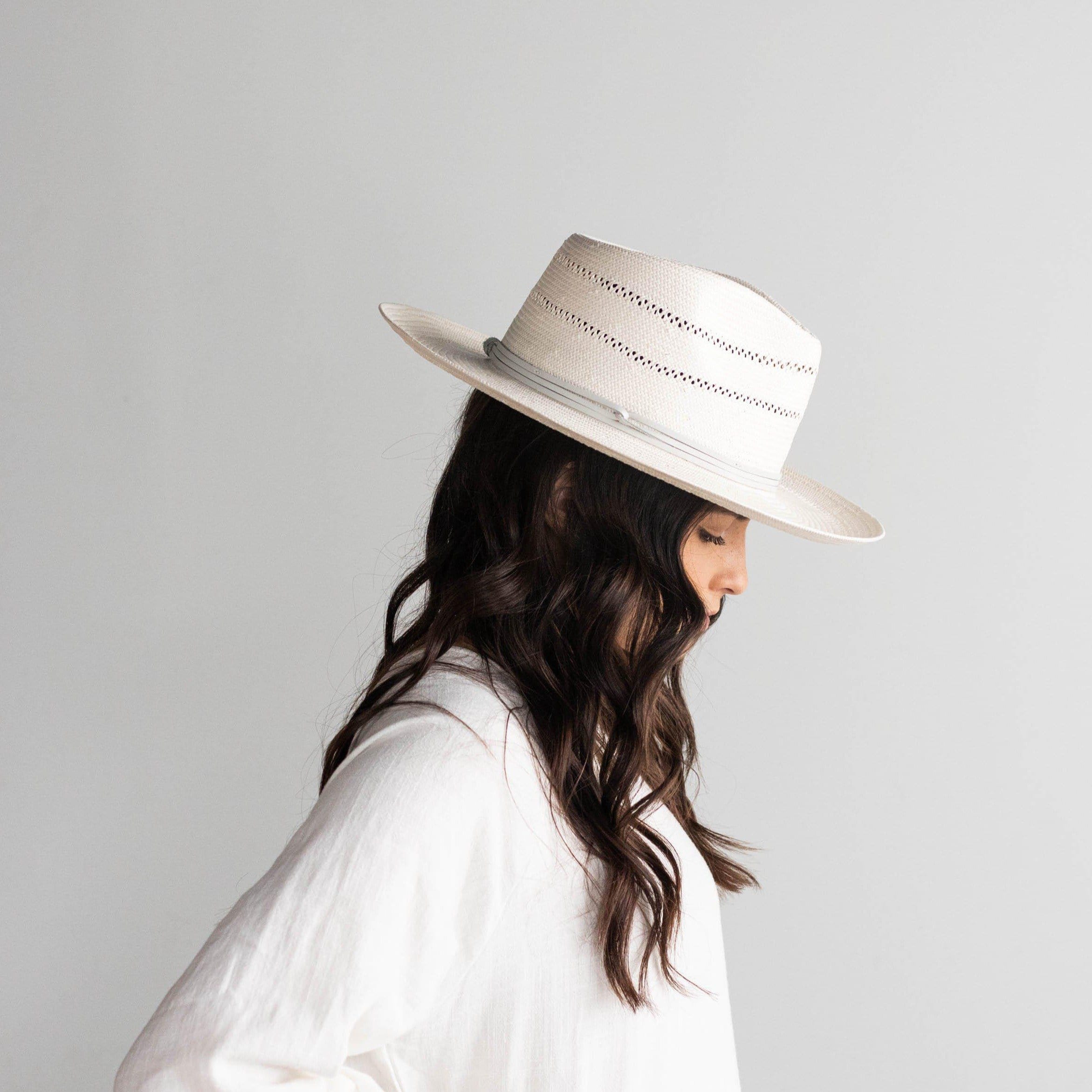 Woman wearing a grey straw fedora hat with a hat band and a white top, facing sideways against a plain background #color_grey