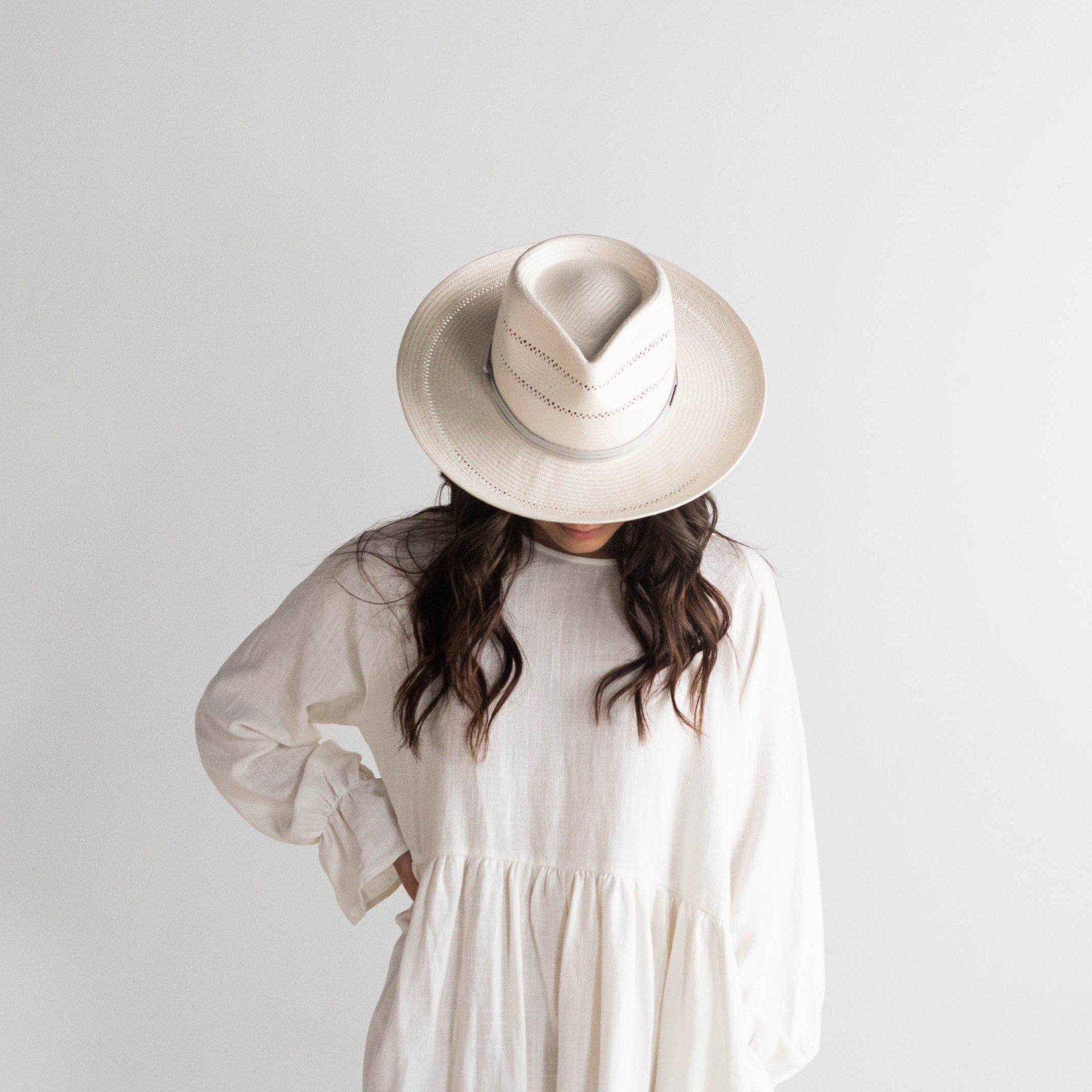 Woman wearing a grey straw fedora hat with a hat band and a white top against a plain background #color_grey