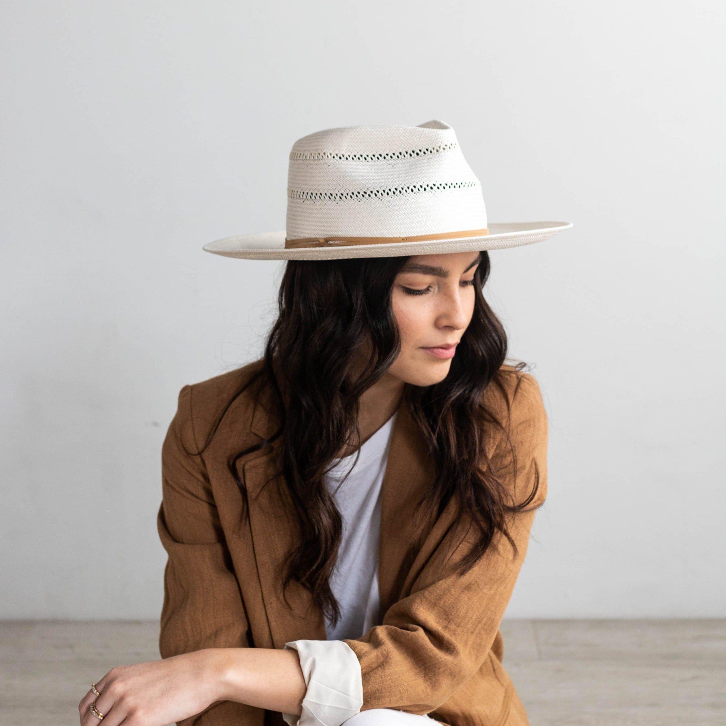 Woman wearing a tan straw fedora hat with a hat band and a white top with a brown coat, facing sideways against a plain background #color_tan
