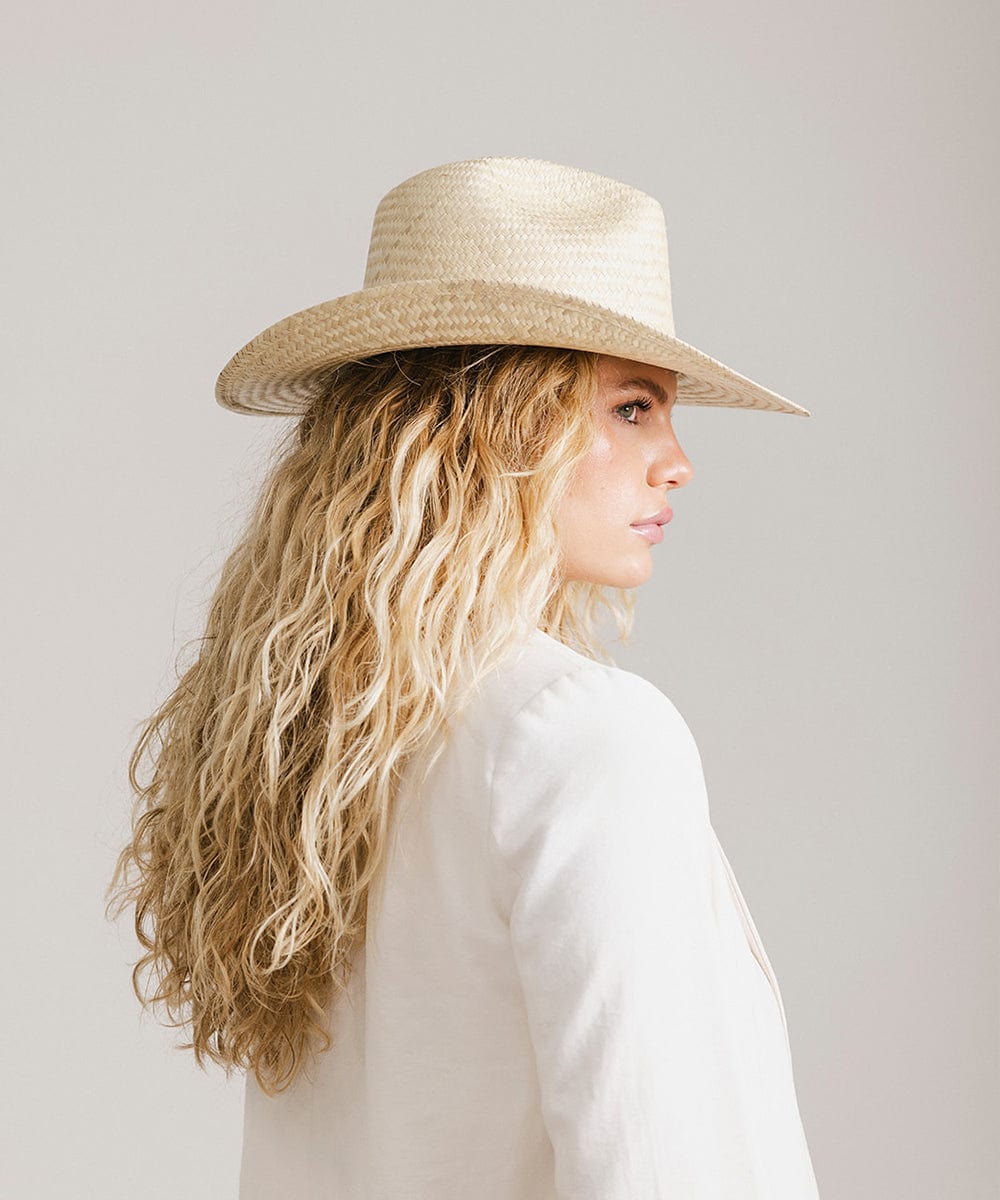 Woman with long blonde hair wearing a natural colored straw cowboy hat and a white jacket, facing sideways  against a plain background  #color_natural