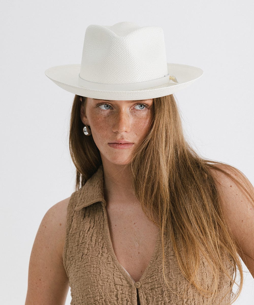 Woman wearing a white straw hat with a hat band and a brown top against a plain background  #color_white