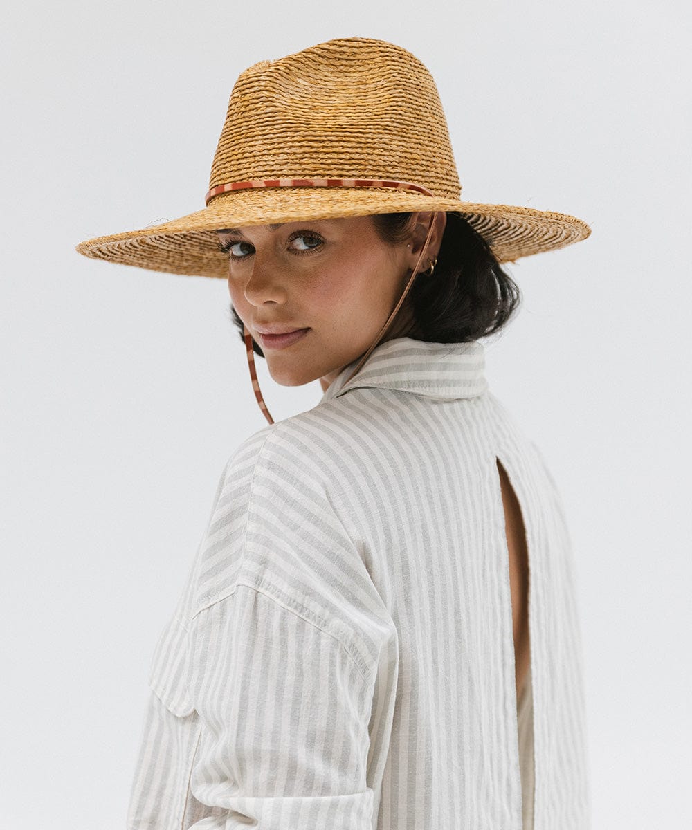 Woman wearing a honey colored straw hat and a light colored shirt against a plain background #color_honey