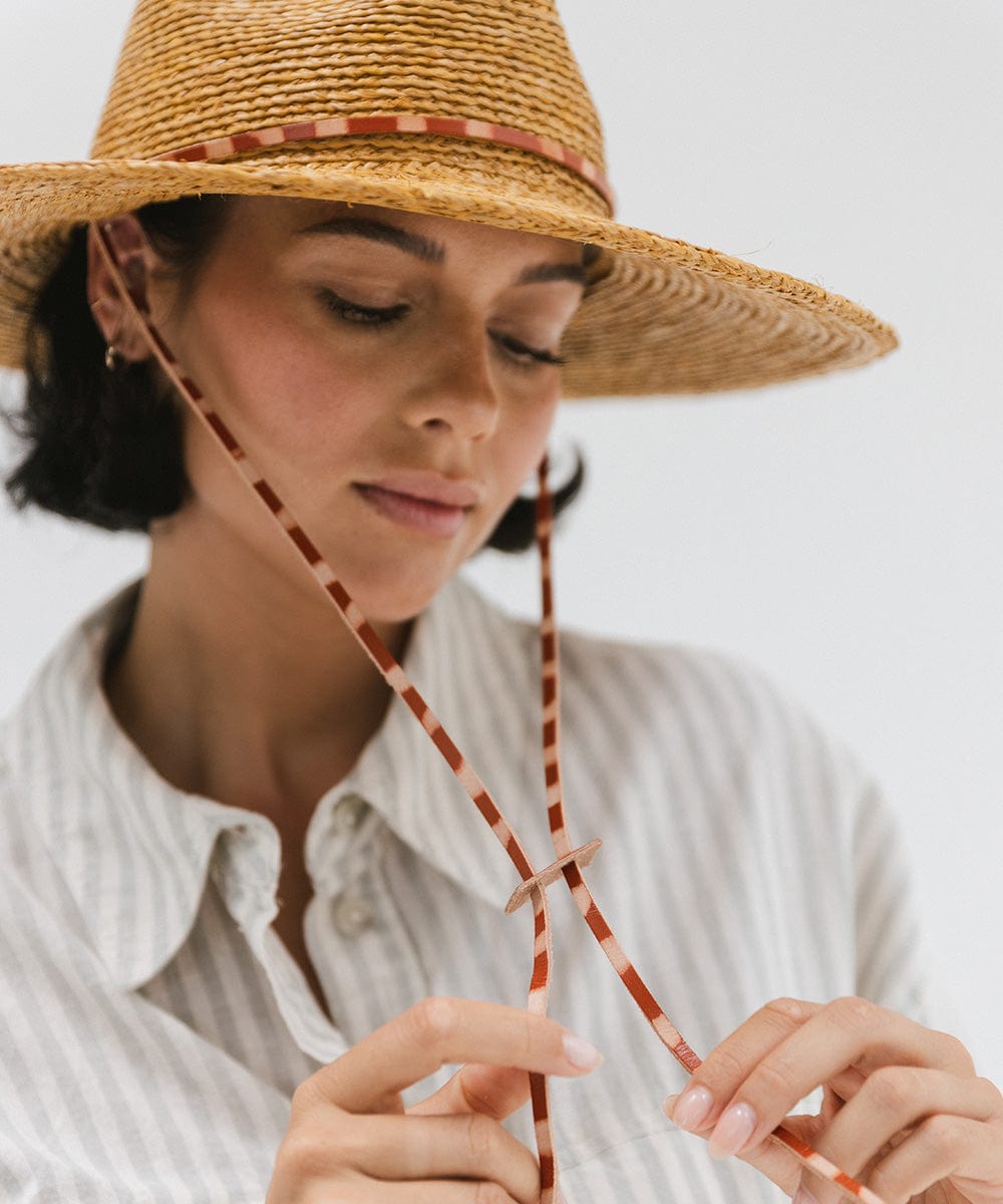 Woman wearing a honey colored straw hat and a light colored shirt, posing against a plain background #color_honey