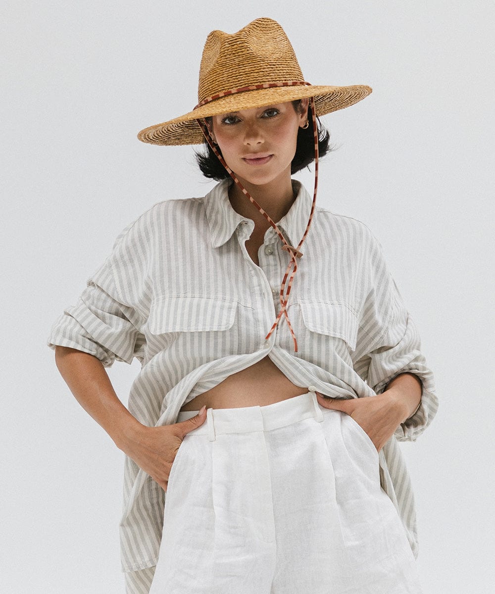 Woman wearing a honey colored straw hat, a light colored shirt and white pants against a plain background #color_honey