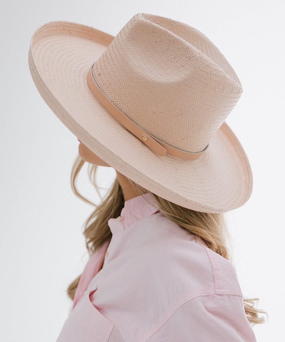 Person wearing a light pink pencil brim straw fedora hat with a hat band, and a pink shirt, facing sideways against a plain background #color_limited edition light pink