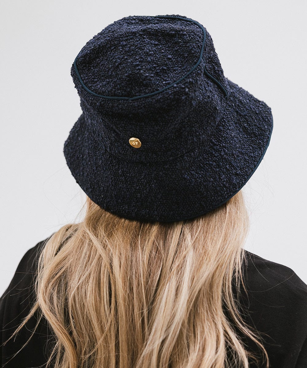 Woman wearing a navy bucket hat and a black t-shirt, facing behind against a plain background #color_navy