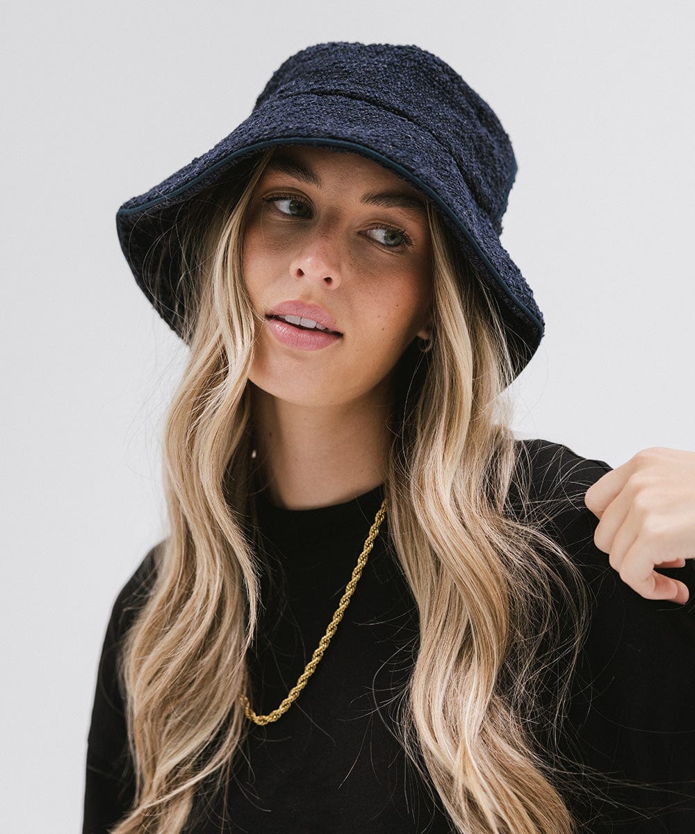 Woman wearing a navy bucket hat and a black t-shirt with a gold chain against a plain background #color_navy