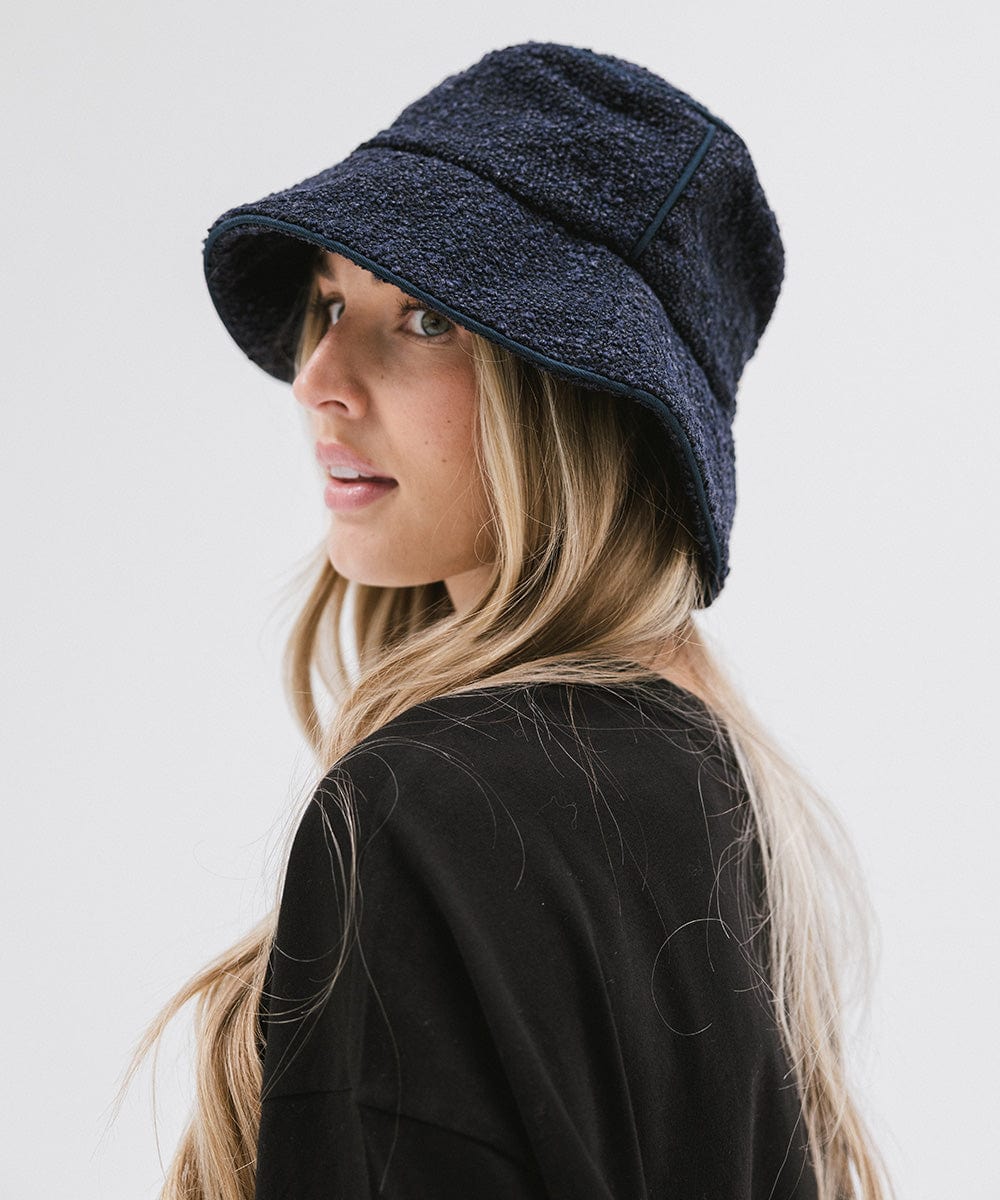 Woman wearing a navy bucket hat and a black t-shirt, posing sideways against a plain background #color_navy