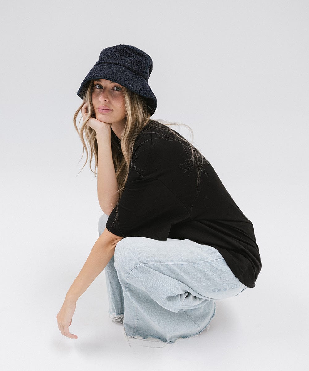 Woman wearing a navy bucket hat, a black t-shirt and light blue jeans, sitting against a plain background #color_navy