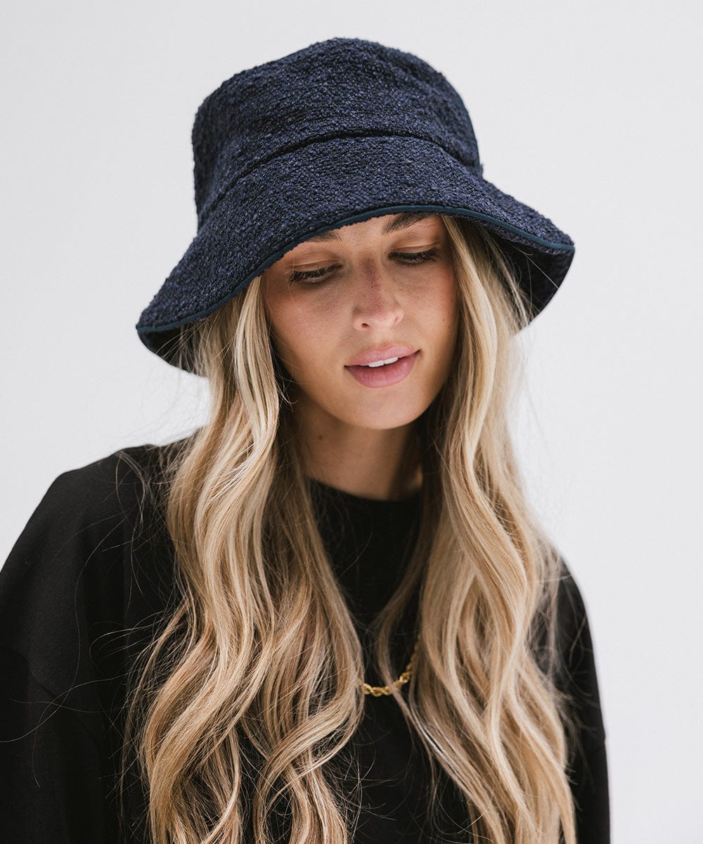 Woman wearing a navy bucket hat and a black t-shirt, looking down against a plain background #color_navy