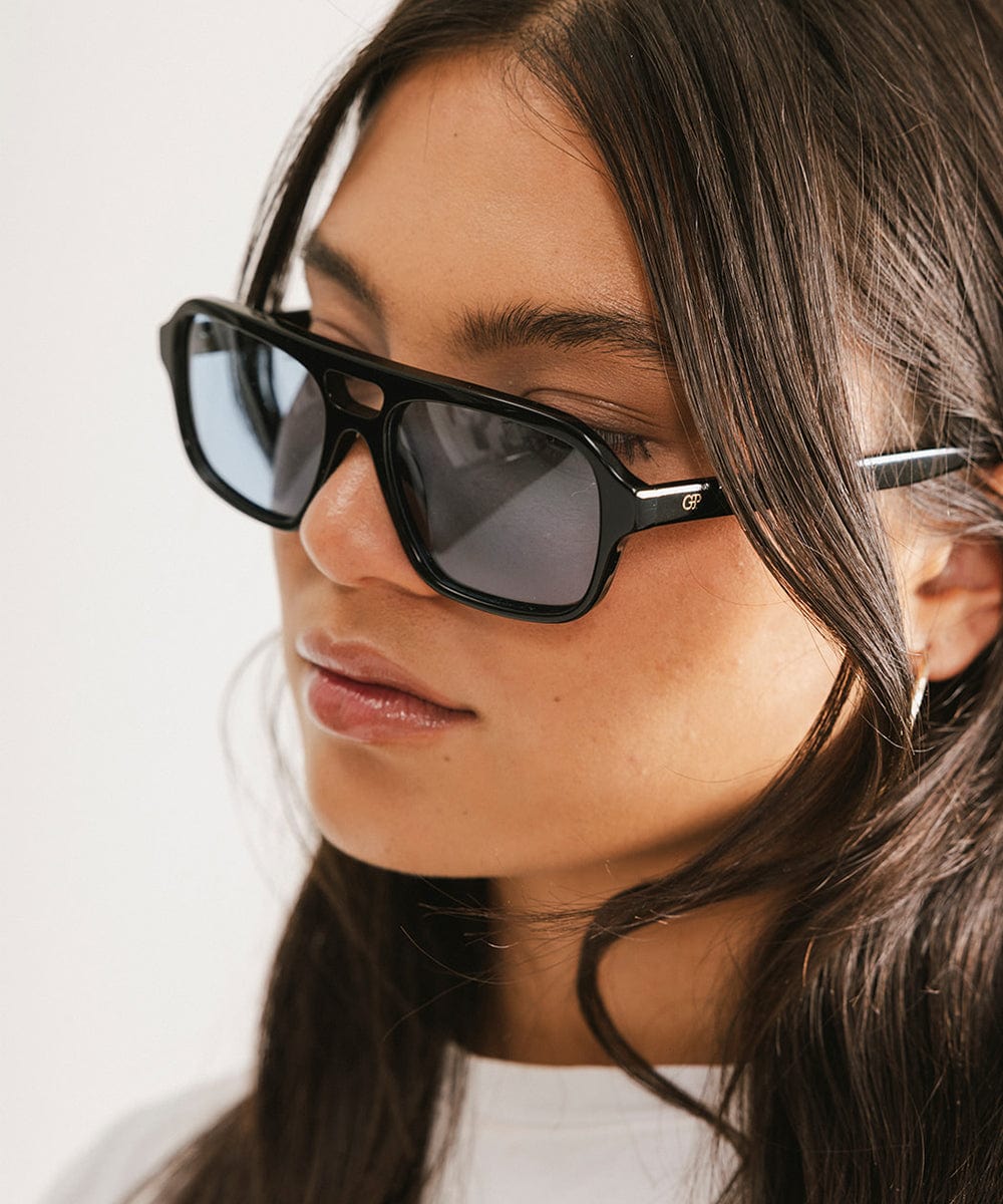 Close up image of a woman wearing black sunglasses against a plain background #color_black