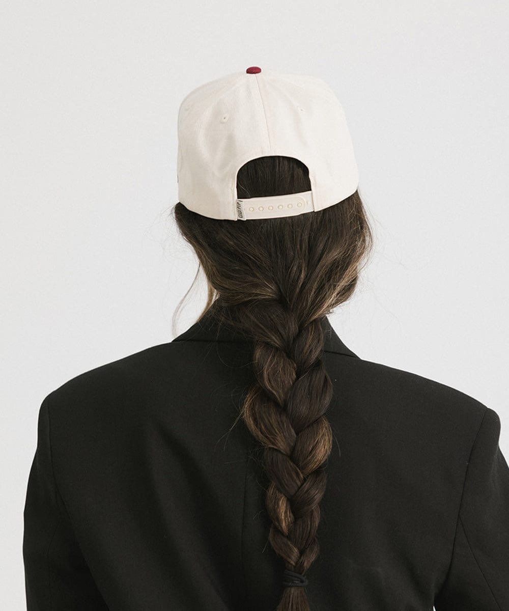 Woman wearing a burgundy Trucker hat and a black coat against a plain background  #color_burgundy