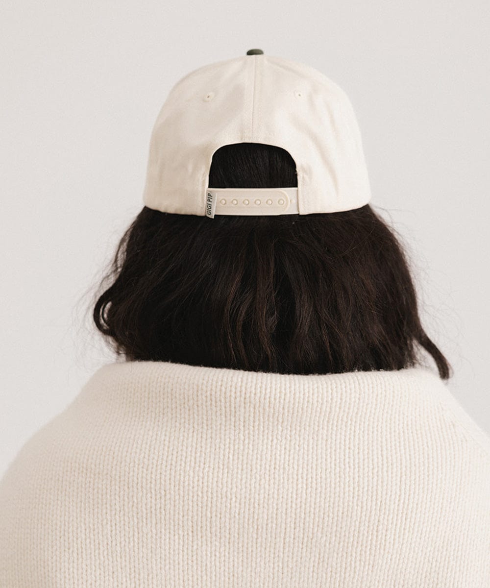 Person wearing a cream and dark green Trucker hat against a plain background  #color_cream - dark green