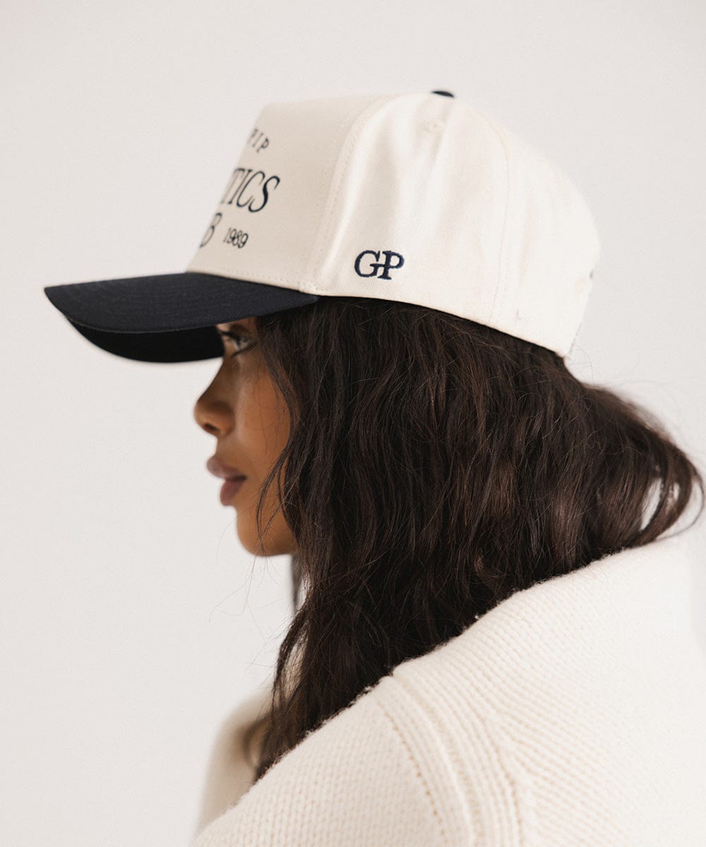 Woman wearing a Navy Trucker hat and a white sweater, facing sideways  against a plain background #color_navy