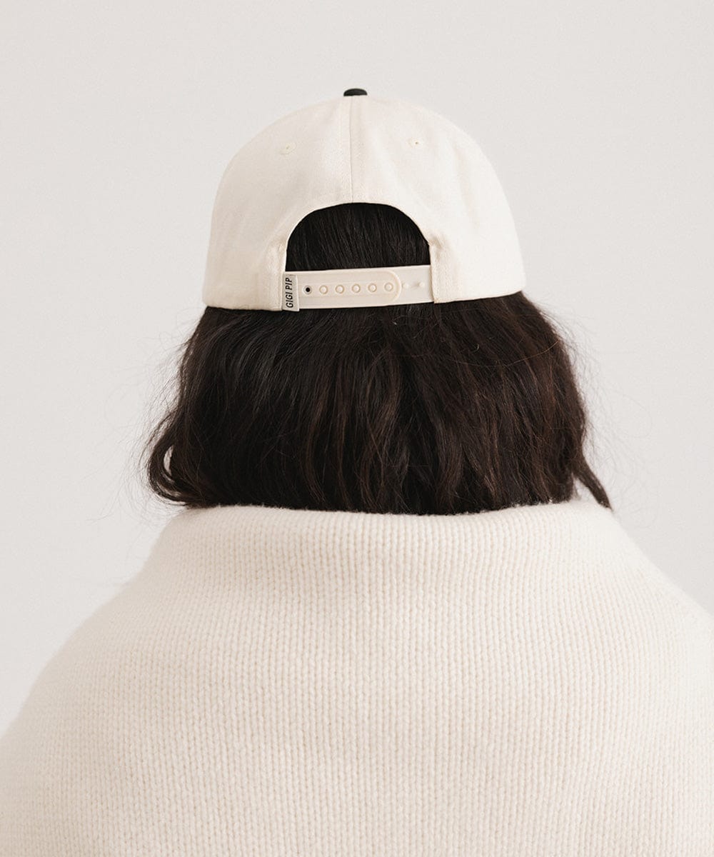 Person wearing a cream and black Trucker hat and a white sweater  against a plain background #color_cream - black