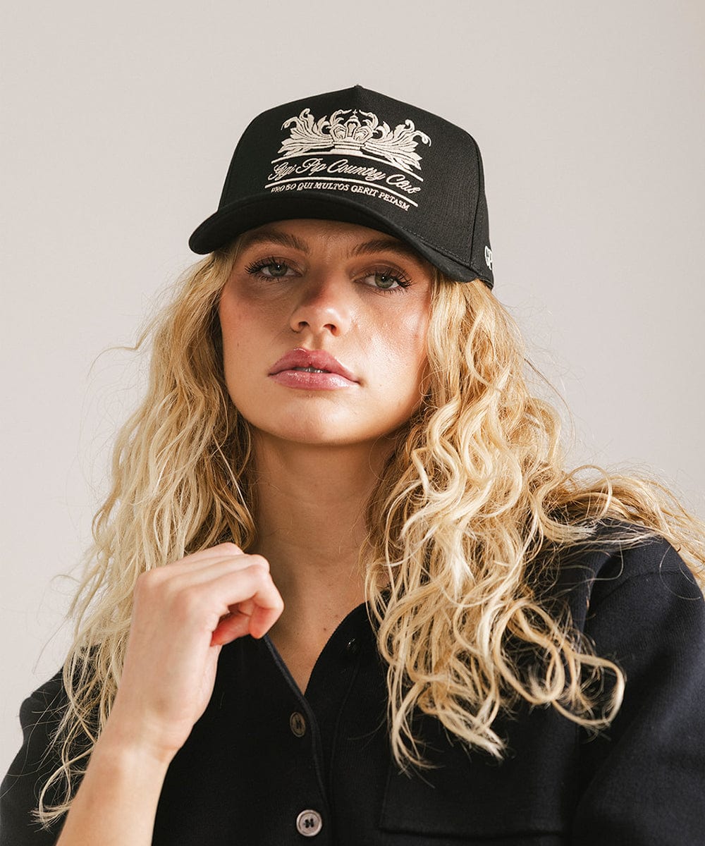 Woman wearing a black vintage trucker cap with a white logo and a black shirt against a plain background  #color_black