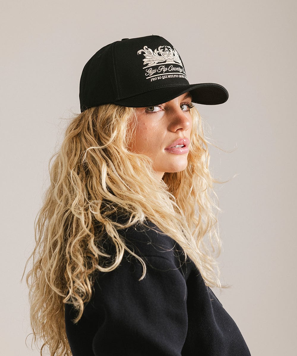 Woman wearing a black vintage trucker cap with a white logo and a black shirt, posing sideways against a plain background  #color_black