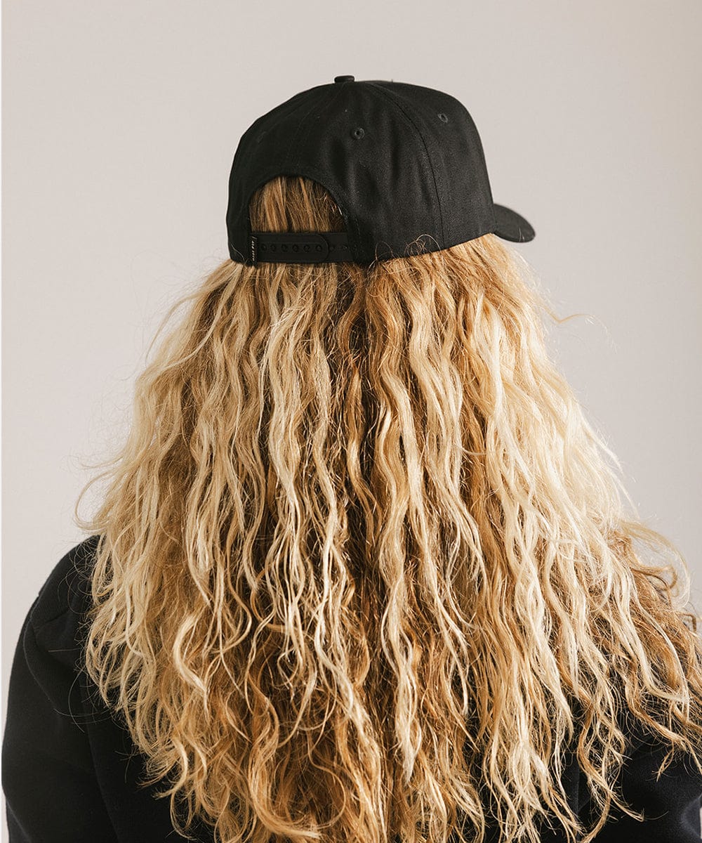 Woman with long hair wearing a black vintage trucker cap against a plain background  #color_black