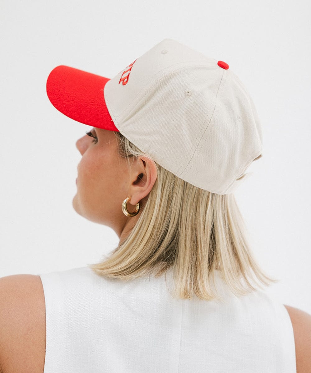 Woman wearing a cream and red trucker hat with 'GIGI PIP' embroidered in red on the front and a white top, posing against a plain background  #color_cream - red