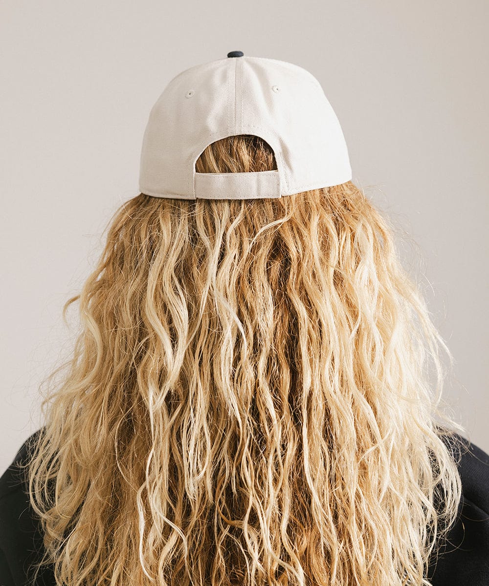 Woman with long hair wearing a cream and navy trucker hat against a plain background  #color_cream - navy