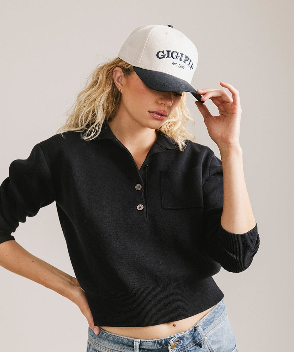 Woman wearing a cream and navy trucker hat with 'GIGI PIP' embroidered in navy on the front and  a black shirt, posing against a plain background  #color_cream - navy