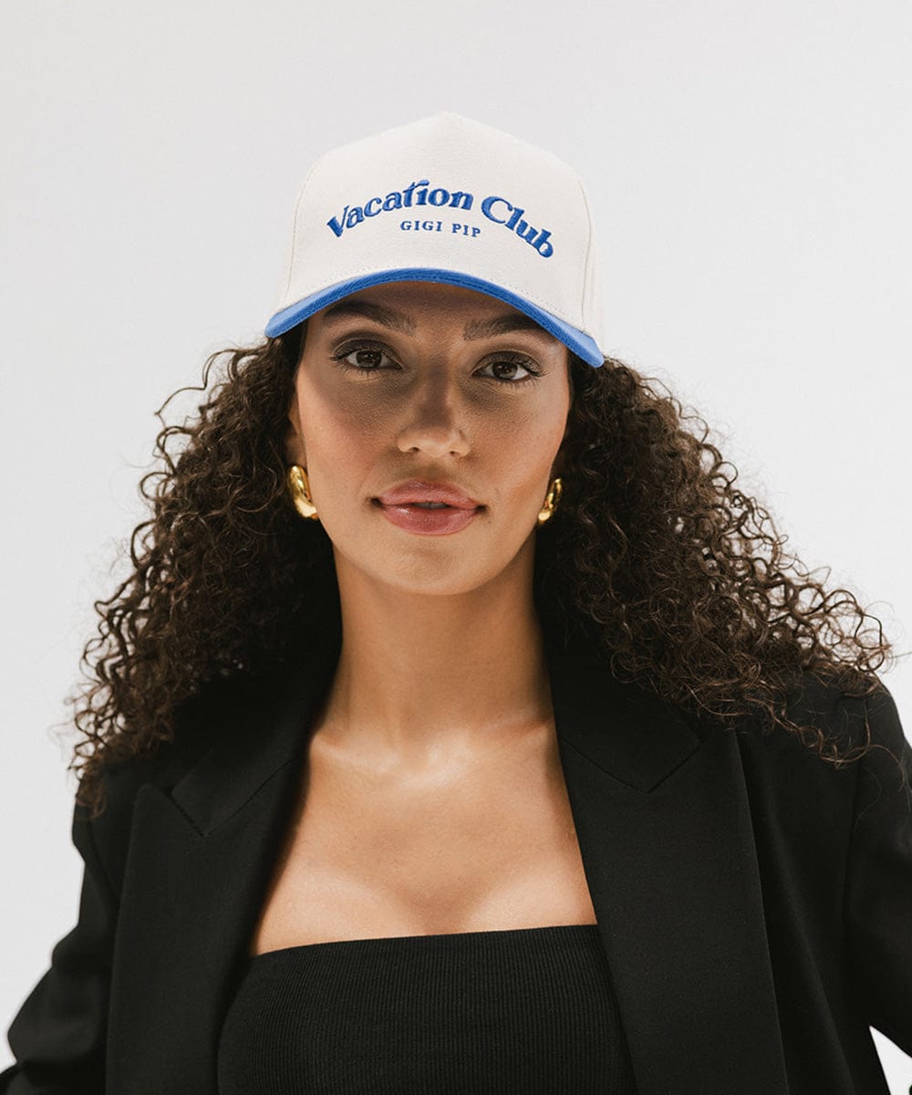 Woman wearing a cream and blue cap with 'Vacation Club' text and a black blazer against a plain background  #color_cream - blue