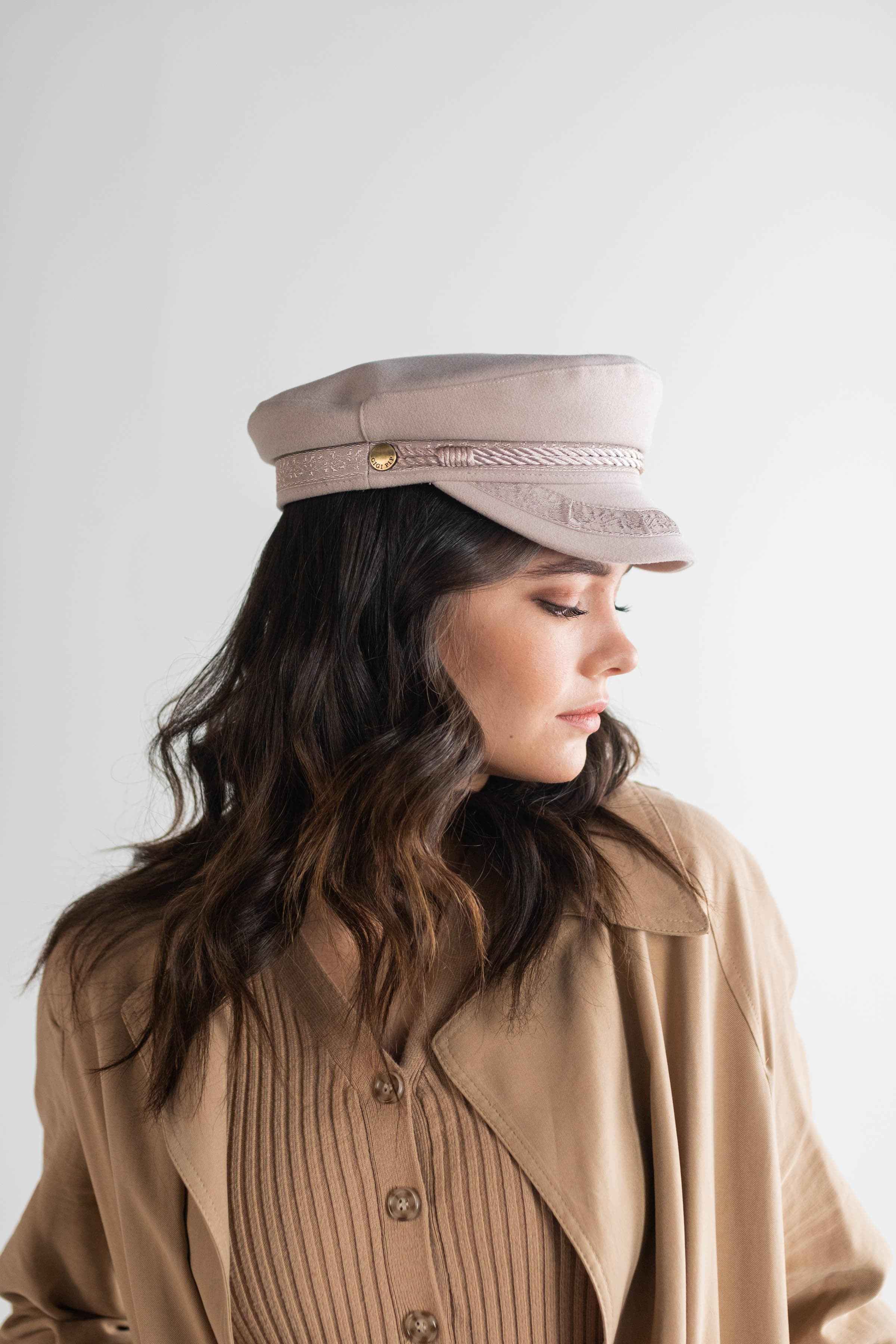 Woman wearing an ivory colored lieutenant cap and a brown shirt with a brown jacket, facing sideways against a plain background #color_ivory