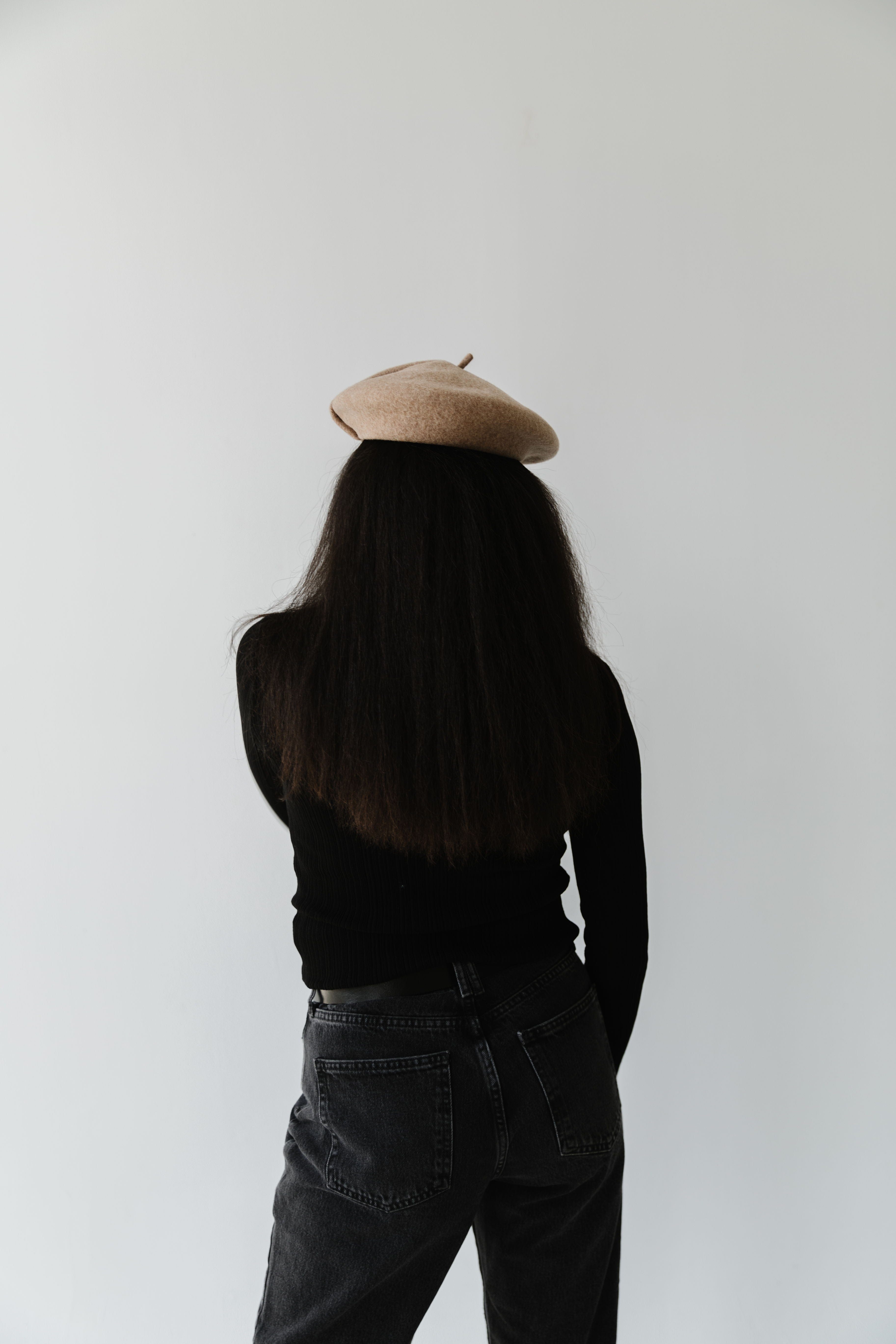 Woman wearing a camel colored beret, a black t-shirt and jeans against a plain background  #color_camel