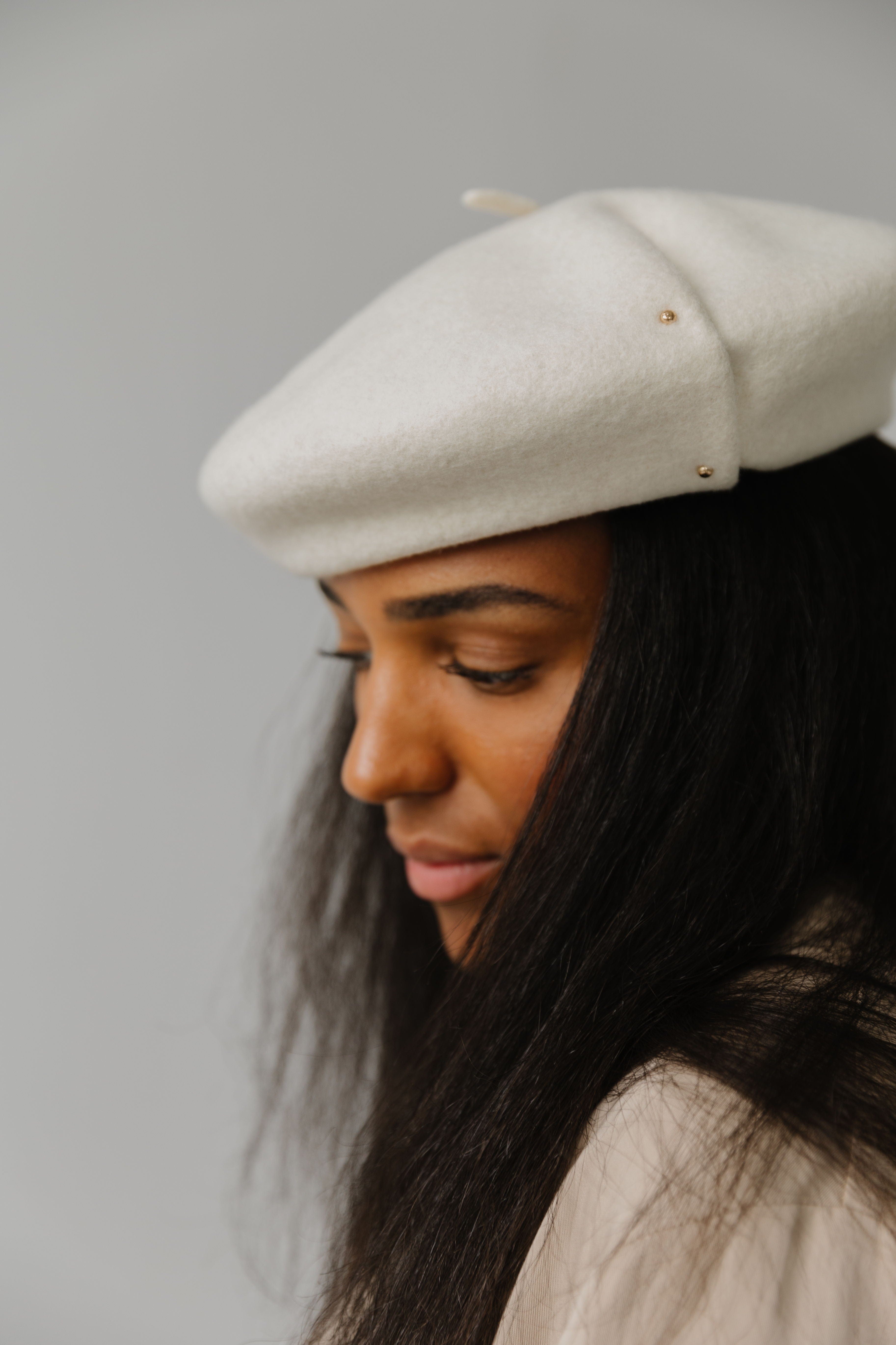 Woman wearing an off white beret facing sideways against a plain background  #color_off white