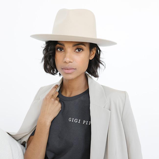 Woman wearing a graphite colored t-shirt with 'GIGI PIP' text, a grey blazer and a cream hat against a white background #color_graphite